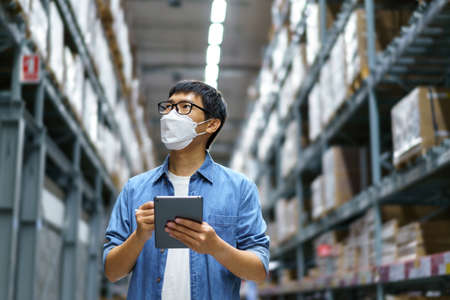 New Normal Asian men, staff, product wearing face mask. counting Warehouse Control Manager Standing, counting and inspecting products in the warehouseの写真素材