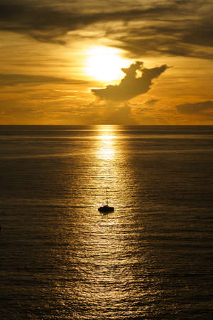Beautiful silhouette of sailboat on sunset at sea with reflection. Summer sun golden hour hot sunset sky.の写真素材