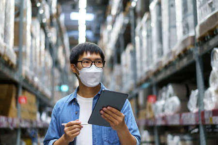 New Normal Asian men, staff, product wearing face mask. counting Warehouse Control Manager Standing, counting and inspecting products in the warehouseの写真素材