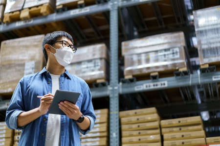 New Normal Asian men, staff, product wearing face mask. counting Warehouse Control Manager Standing, counting and inspecting products in the warehouseの写真素材