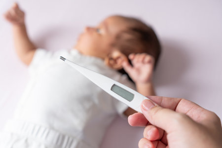 A mother gently checks her baby temperature with a thermometer, ensuring her little one is comfortable and healthy, with tender care and concern.の写真素材