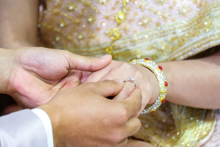 Thai wedding groom's hand putting a wedding ring on the bride's finger.の写真素材