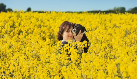 Woman with dog on arms in a rape field.の写真素材