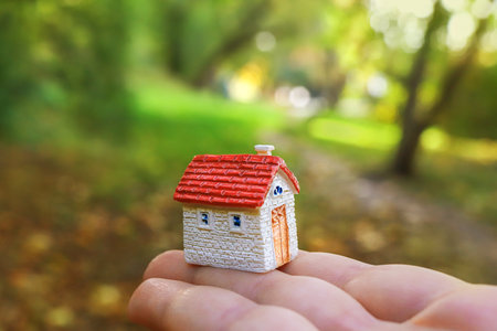 A small model of the house stands on the arm. The background green of the forest and the trees. Symbol of building a house in nature.の写真素材