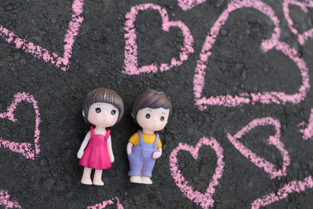 Toys boy and girl teenagers lie on a dark background. Pink hearts are drawn around them. The concept of the first relationship and falling in love. Valentines Day.の写真素材