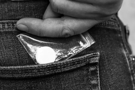 large white tablet in transparent bag. guys hand pulls drugs out of jeans pocket. Criminal illegal...