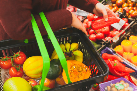 female customer with grocery basket is shopping for fruits and vegetables in supermarket. Healthy eating and vegetarian diet.の写真素材
