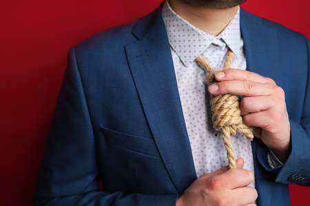 businessman in blue suit pulls noose knot around his neck instead of tie. symbol of collapse of business, loans, debts and failures.の写真素材