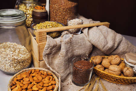 Variety of cereals and nuts on table. Walnuts, almonds, wheat grains and ears of corn in cans and...