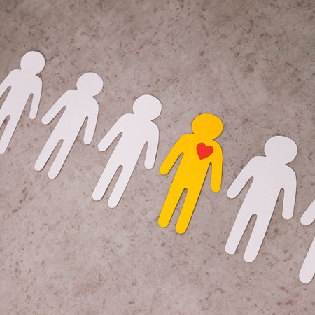 Cut out of white paper figures of people in line. In center is yellow man, with red heart in chest. Falling in love. symbol of meaning of life and human existence.の写真素材