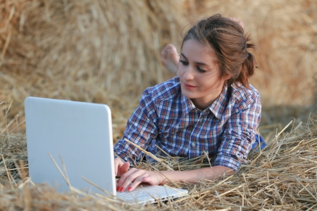 Country girl with laptop sitting at haystack looking to cameraの写真素材