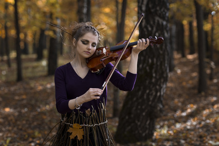 Half-body size portrait of young woman playing violin over the fall park backgroundの写真素材