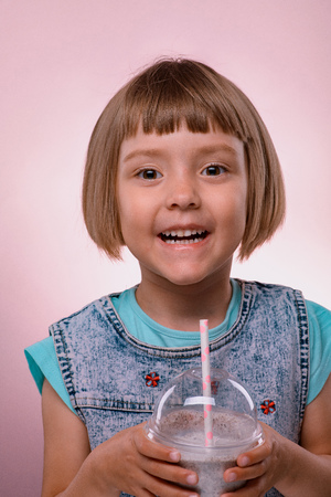 Little girl drinks milkshake on pink backgroundの写真素材