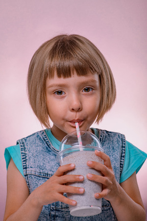 Little girl drinks milkshake on pink backgroundの写真素材