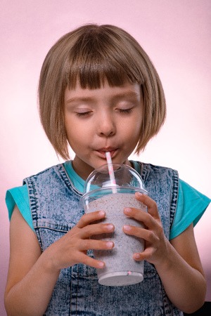 Little girl drinks milkshake on pink backgroundの写真素材