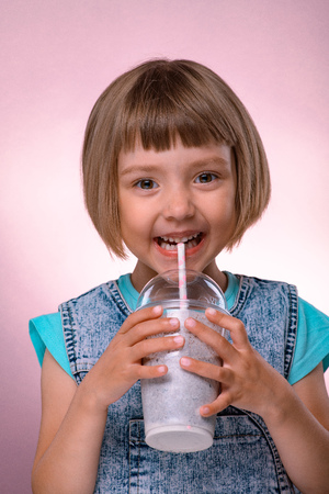 Little girl drinks milkshake on pink backgroundの写真素材