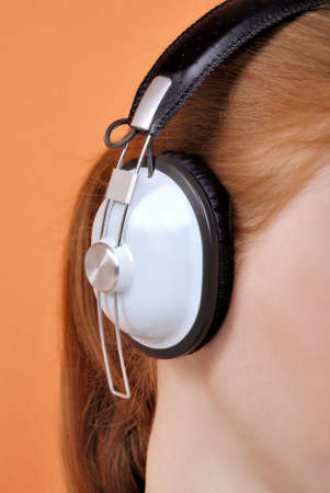 Redhead young woman in headphones on an orange backgroundの写真素材