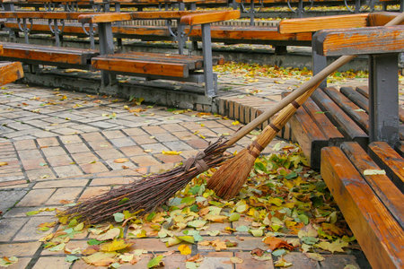 Broom and the broom standing near the bench area in the autumn. Cleaning street from the park autumn...