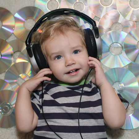 A little boy in headphones listens to music. White Boy in headphones lying on disks. Baby listening...