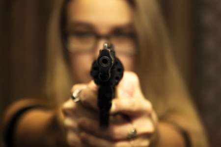 A girl with white hair and a gun in her hands is aiming at the camera, self-defense, attack, weapons. selective focus.の写真素材