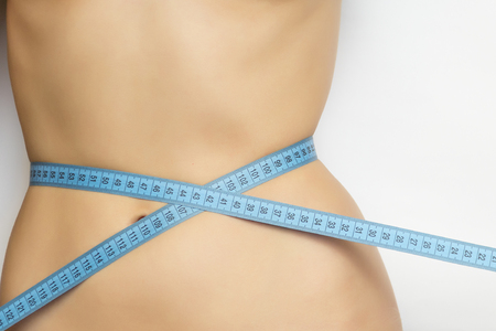 A beautiful, athletic, young girl measures her waist. Without a T-shirt on a white backgroundの写真素材