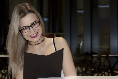 A beautiful girl with white hair and wearing fashionable glasses reads the menu in the restaurantの写真素材
