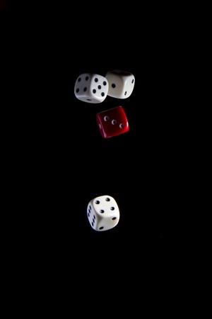 three white and one red dice on a black background during a free fallの写真素材