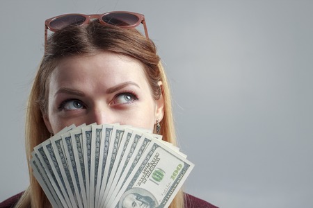 A girl in a burgundy sweatshirt covers her face with hundred-dollar bills.の写真素材