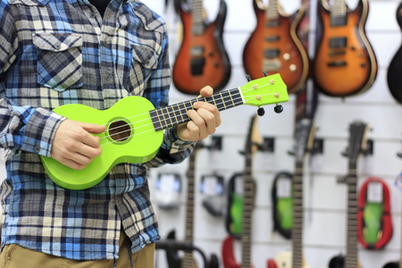 Portrait of a bearded hipster male in red hat playing on ukuleleの写真素材