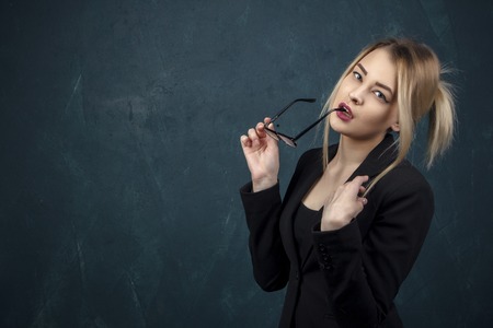 Portrait of a beautiful woman with sunglasses in hands and suit against a blue textural wall with place for text.の写真素材