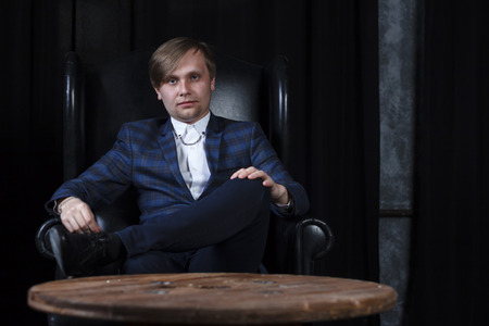 A young man in a suit on the background of an expensive dark interior with a place for advertising or text.の写真素材
