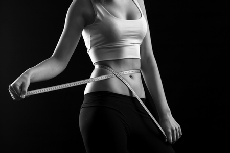 Happy fitness girl measuring her waistline over black background. black and whiteの写真素材
