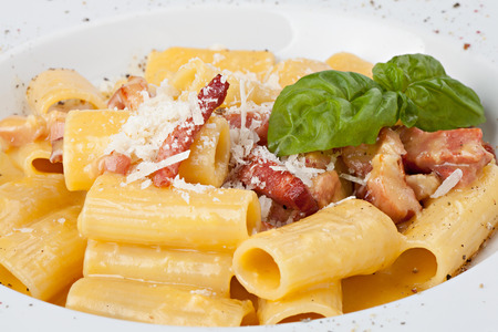 Close-up italian rigatoni plate with prosciutto, parmesan cheese and leaf basilの写真素材