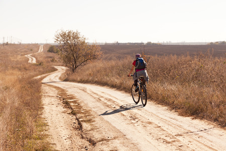 Woman riding a mountain bike on a rural  road, back view.の写真素材