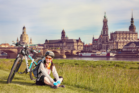 Adult attractive female cyclist sitting  on the grass and resting. The happy woman sits  at the old city background and  looks at the camera. So-called  The Balcony of Europe, Dresden, Germanyの写真素材