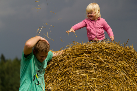 healthy childhood in harmony with nature - happy girl sits on a haystack in a wheat fieldの写真素材