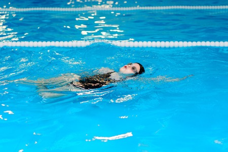 swimming lessons for children in the pool - beautiful fair-skinned girl swims in the waterの写真素材