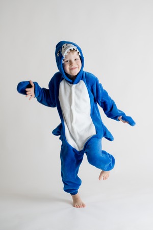 cheerful little boy posing on a white background in pajamas kigurumi, blue shark costumeの写真素材