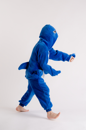 cheerful little boy posing on a white background in pajamas, blue shark costumeの写真素材