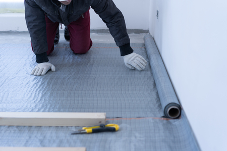 master carpenter mounts pine wood floor - eco-friendly flooring. gluing the insulation layer under the lag on the concrete