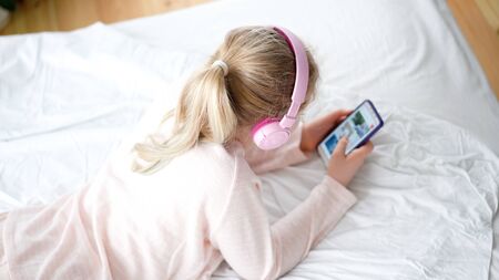 modern life of generation Z. teenage girl in pajamas and headphones in the room on the bed listens...