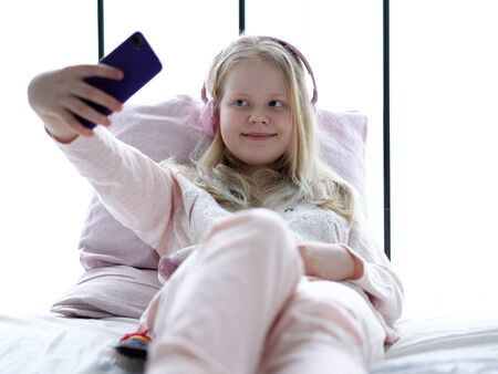 modern life of generation Z. teenage girl in pajamas and headphones in the room on the bed listens to music from a smartphone.の写真素材