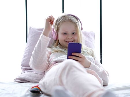 modern life of generation Z. teenage girl in pajamas and headphones in the room on the bed listens to music from a smartphone.の写真素材