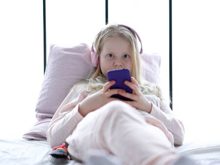 modern life of generation Z. teenage girl in pajamas and headphones in the room on the bed listens to music from a smartphone.の写真素材