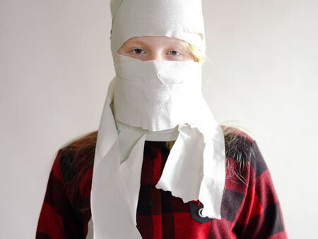 funny photo - quarantined due to an epidemic of coronavirus. girl in a mask from toilet paper posing on a gray background.の写真素材