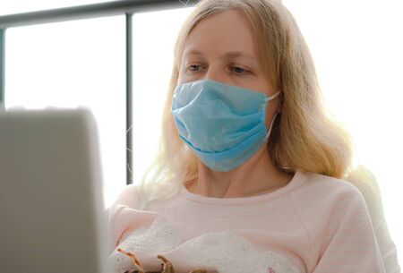 quarantine for coronavirus epidemic. An infected masked woman works at home with a laptop.