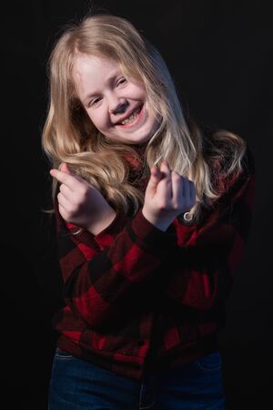 happy schoolgirl posing in studio on a black background - shows hands signs heartsの写真素材