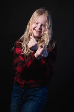 happy schoolgirl posing in studio on a black background - shows hands signs heartsの写真素材