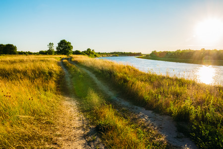 Landscape with dirt road in the field with sunset on the riverの写真素材