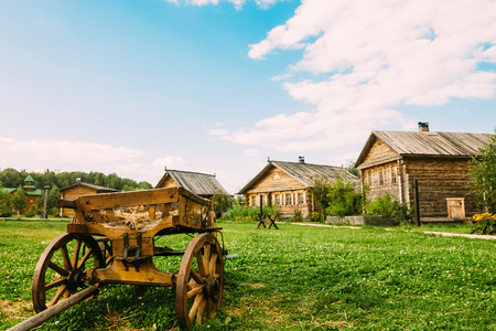 Old wooden cart on the green grass in rural areas. Summer day with a beautiful sky and white cumulus cloudsの写真素材